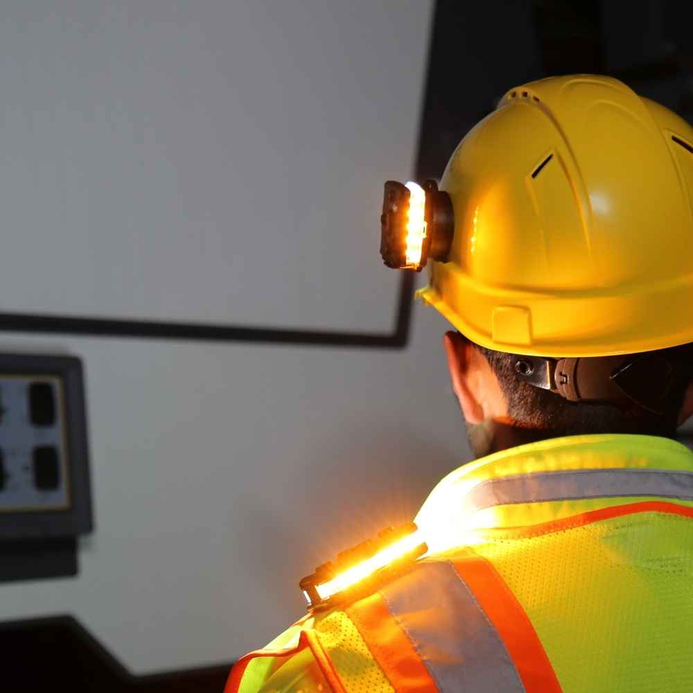 Person wearing a hard hat and high-visibility jacket with a Guardian Angel Magnetic Hard Hat Earmuff Mount in a dark setting.