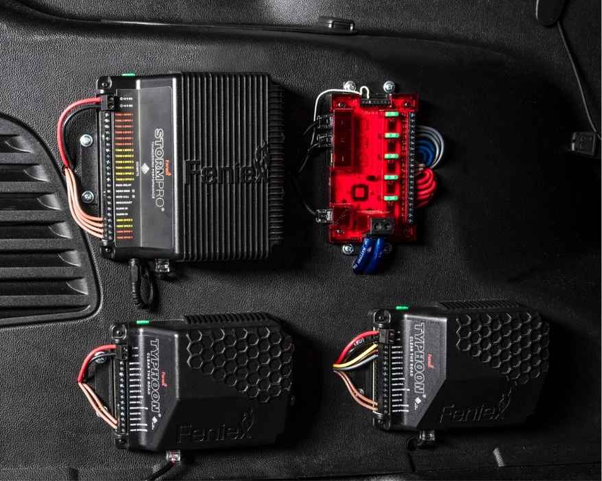 Automotive Feniex Storm 200W Siren on a black car mat with 'Feniex' branding.