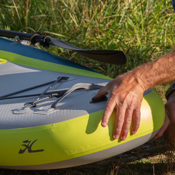 Hand touching a lime green and gray inflatable paddleboard with grass in the background
