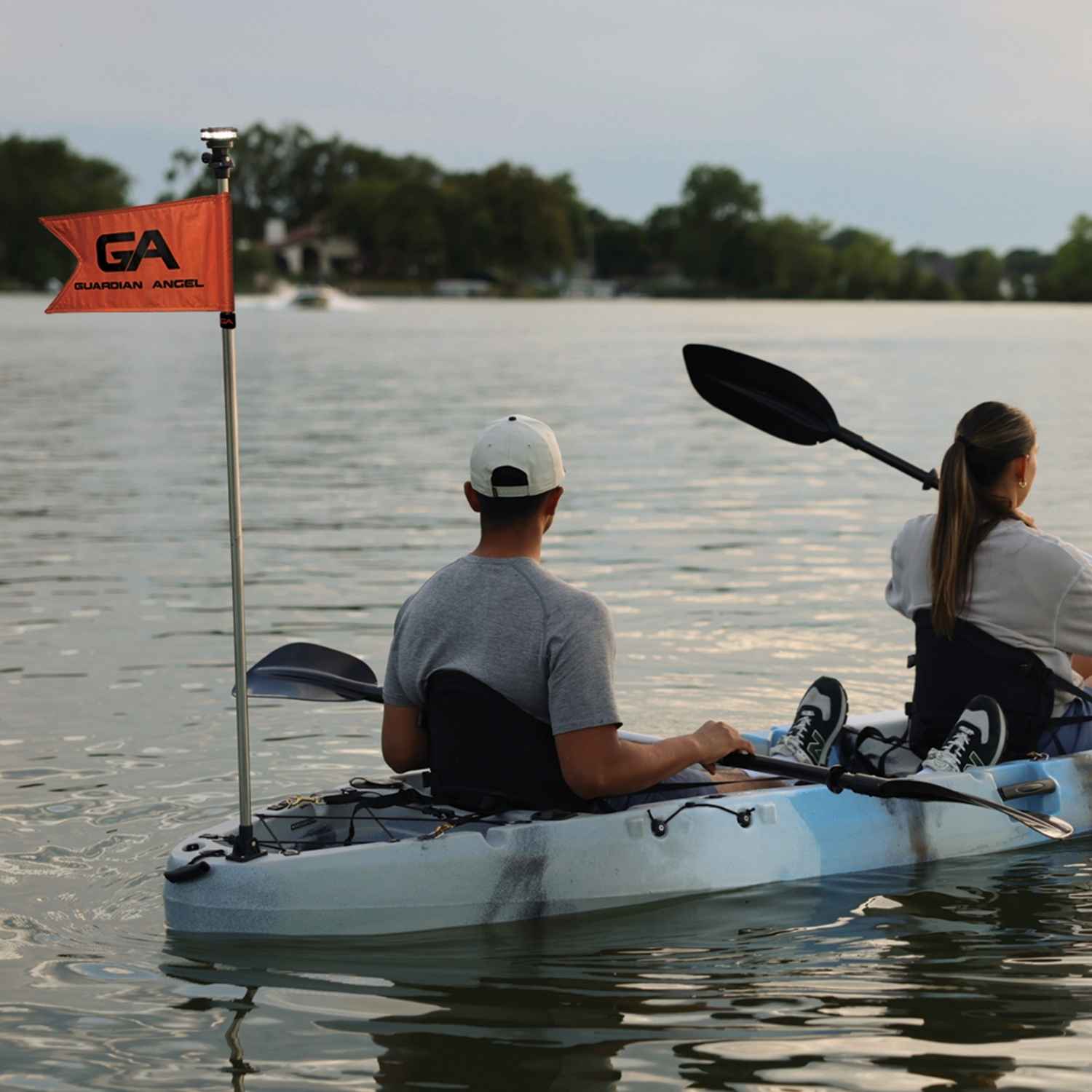 Two people in a kayak on water with a 'GA' flag in the foreground.